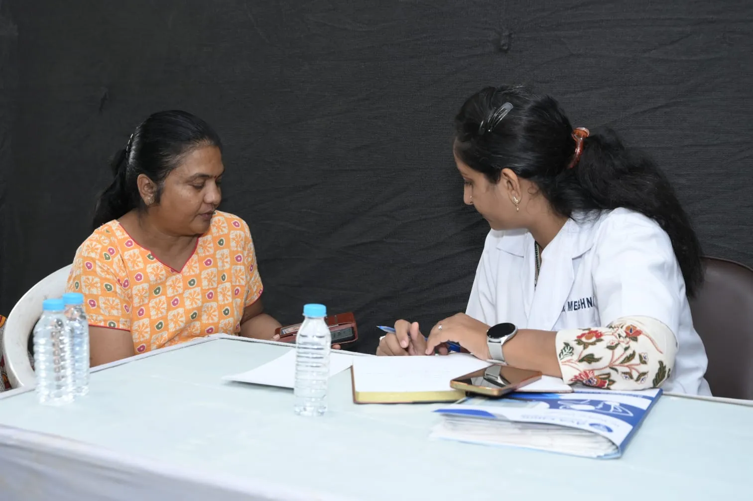 Dr. Meghna Oza taking notes while consulting a woman at a health camp