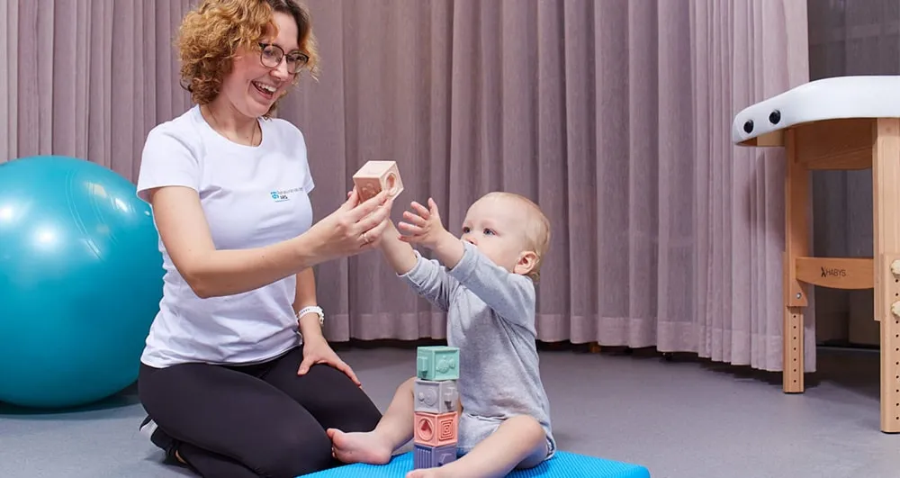 Therapist using toys to help a toddler practise sitting balance and reaching
