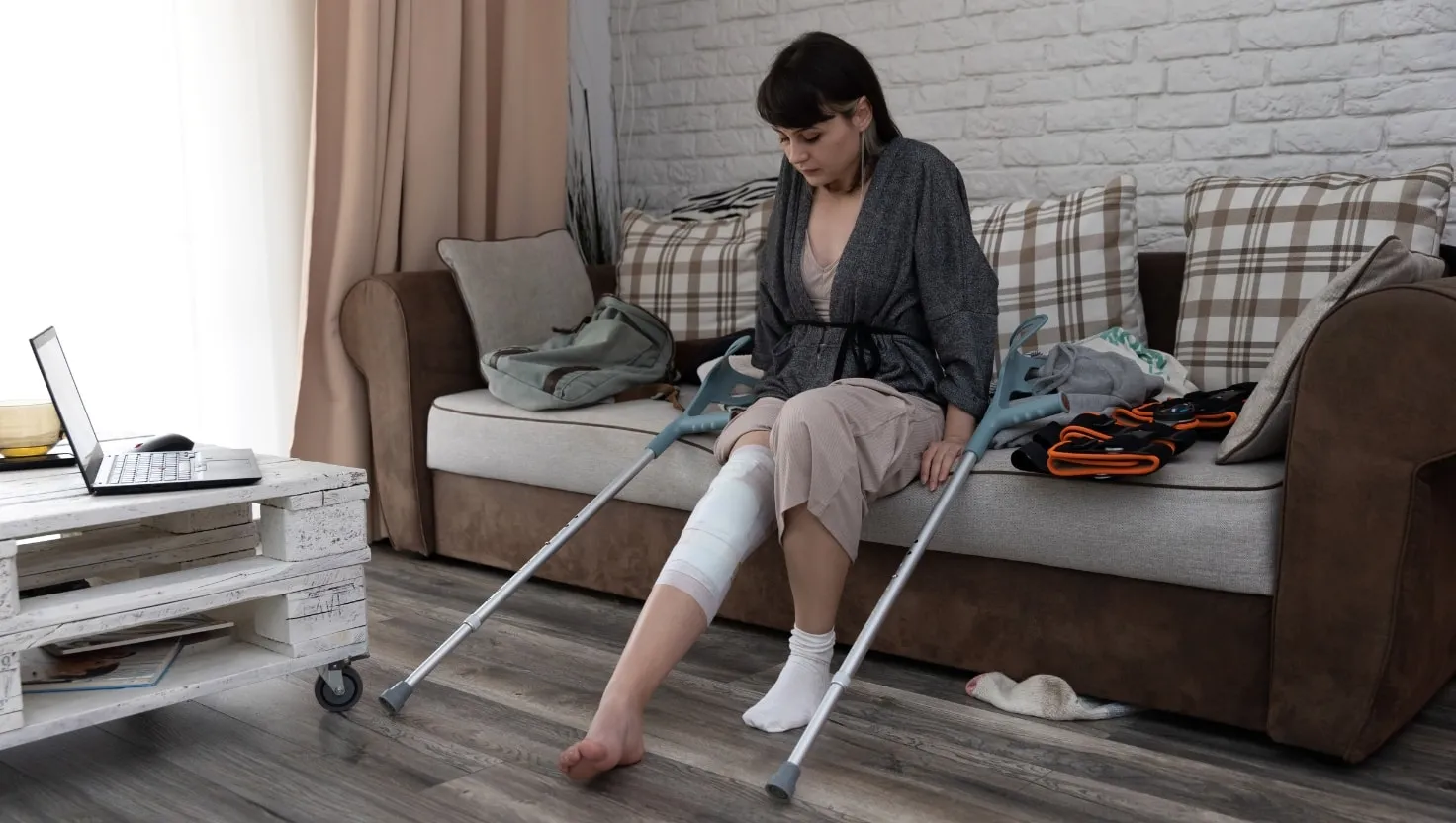 Woman with a knee brace using crutches to stand up from a sofa at home